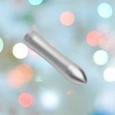 A sleek, silver Doxy Bullet Vibrator - Silver by Doxy with a rounded tip is set against a softly blurred background filled with colorful, out-of-focus lights, creating a festive and ethereal atmosphere perfect for precision play.